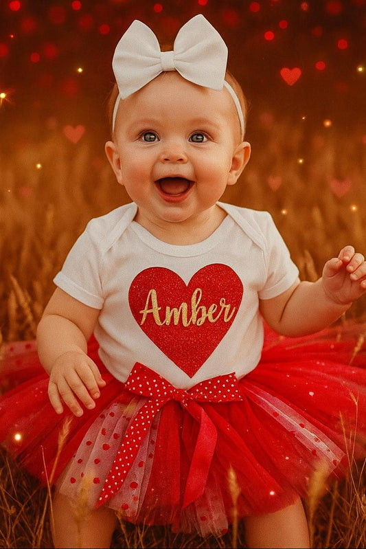 Baby in a red and white outfit with a heart design and the name 'Amber', standing in a field with heart-shaped lights.